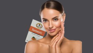 a close shot of a beautyful face women with glowing skin smiling,turmericsoap pack is peeking from her shoulder.